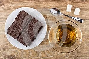 Wafer in chocolate, tea on saucer, sugar, teaspoon on table