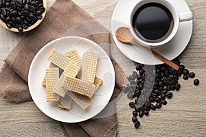 Wafer with coffee flavored cream in white plate with cup and coffee bean background.Top view