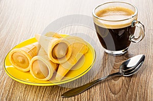 Wafer horns with cream in saucer, cup with black coffee, spoon on table