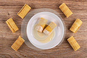 Wafer rolls with condensed milk in saucer, few wafer rolls on table. Top view