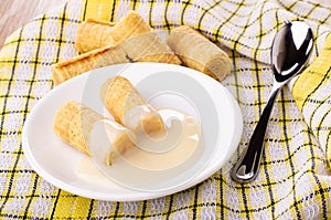 Wafer rolls with condensed milk in saucer, wafer rolls on napkin on table