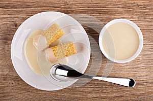 Wafer rolls with condensed milk, spoon in saucer, bowl with condensed milk on table. Top view