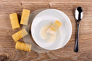 Wafer rolls, roll with condensed milk in saucer, spoon on table. Top view