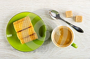 Wafer rolls in saucer, spoon, sugar, cup with coffee on table. Top view