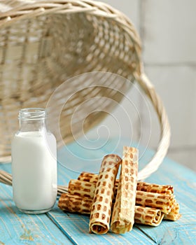 Wafer rolls or tubes and milk in glass jar on wooden table. Sweet rolls filled or stuffed with condensed milk. Soft