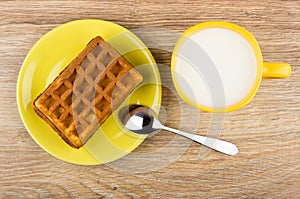 Wafer stuffed in yellow saucer, cup of milk and spoon