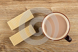 Wafers, brown cup of cocoa with milk on wooden table. Top view