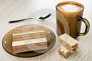 Wafers in brown saucer, spoon, cappuccino in cup, pieces of wafer on wooden table