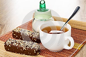 Wafers in chocolate with peanut, sugar bowl, spoon in cup with tea on mat on wooden table