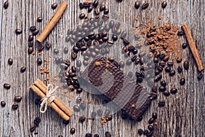 Wafers in chocolate on a wooden table with coffee beans and cocoa powder. View from above.