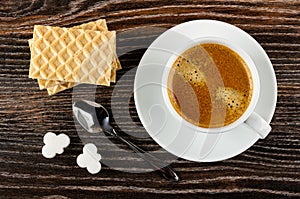 Wafers, cup with black coffee on saucer, pieces of sugar, spoon on wooden table. Top view