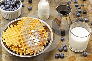 Wafers in metal bowl. Berries in white bowl. Milk in glass. Cezve and blueberries on table