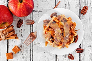 Waffle with baked autumn apples, pecans and caramel, above view table scene over a white wood background