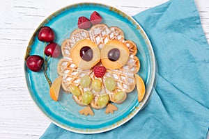 Waffle with fruits and berries in the shape of cute owl with balloons, food for kids idea, top view