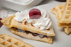 waffle in shaped heart with chantilly cream and raspberry in a white plate