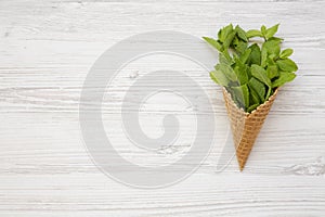 Waffle sweet ice cream cone with mint on white wooden background, top view. Flat lay, overhead, from above