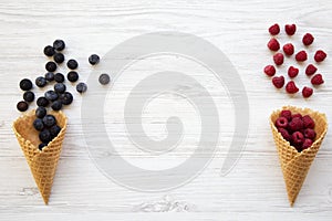 Waffle sweet ice cream cones with raspberries and blueberries over white wooden background, top view. Flat lay.