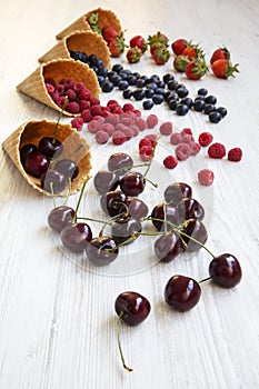 Waffle sweet ice cream cones with raspberries, cherries, strawberries and blueberries over white wooden background