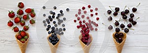 Waffle sweet ice cream cones with raspberries, cherries, strawberries and blueberries over white wooden background, view from abov