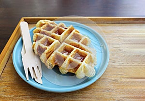 Waffle topped with honey sauce on blue plate at cafe. Sweet bakery on dish.