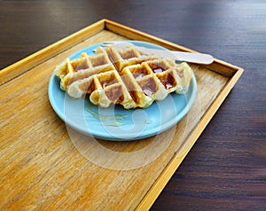 Waffle topped with honey sauce on blue plate at cafe. Sweet bakery on dish