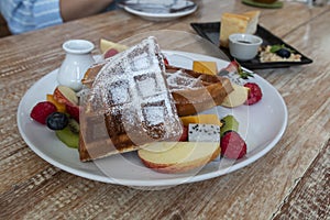 Waffle topped with mixed fruits, syrup, whipped cream, icing sugar and freshly chopped berries.