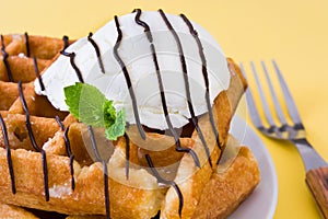 Waffles with chocolate sauce, ice cream and mint on yellow background