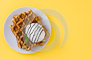 Waffles with chocolate sauce, ice cream and mint on yellow background