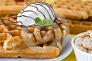 Waffles with chocolate sauce, ice cream and mint on yellow background
