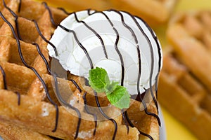 Waffles with chocolate sauce, ice cream and mint on yellow background