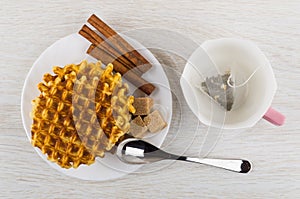 Waffles, cinnamon, sugar cubes in plate, cup with tea bag