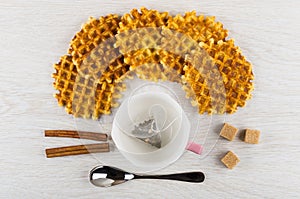 Waffles, cup with teabag, cinnamon, sugar cubes, spoon on table