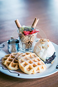 Waffles dusted with icing sugar and iceream and fruit on the side