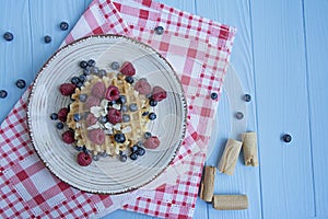 Waffles with fresh banana, raspberries, blueberries for breakfast. Belgian waffles. Light wooden background