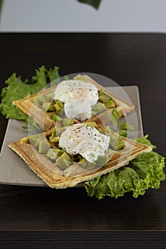 Waffles with pouched eggs, avocado and lettuce on a wooden table