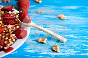 Waffles with strawberry on white plate on blue background.