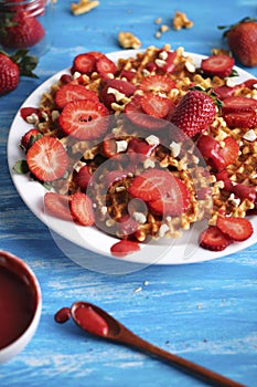 Waffles with strawberry on white plate on blue background.