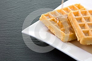 Waffles with syrup coming from above on a white plate on the rig