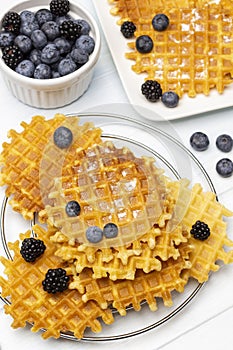 Waffles on the table and on the plate. Blueberries and blackberries in a bowl