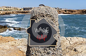 Wage gap symbol. Concept words Wage gap on wooden blocks on a beautiful black chalk blackboard on a beautiful beach stone blue sea