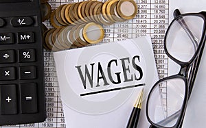 WAGES - word on a white piece of paper on the background of a calculator, pennies and glasses