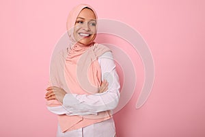 Waist-length portrait of beautiful Arabic Muslim woman in pink hijab posing looking to the side with attractive gaze, toothy smile