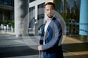 Waist length portrait of a handsome successful businessman developer entrepreneur in business suit with a luggage standing outdoor