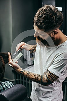 Waist up of bearded barber cutting hair of his client