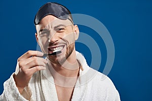 Waist up of Caucasian young man brushing his teeth against blue background