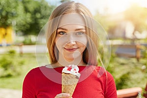 Waist up of freckled green-eyed girl with dimples standing with ice-cream against green nature background admiring sunshine and fr