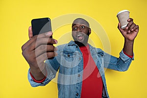 Waist up of funny African man keeping cupholder and smartphone in arms