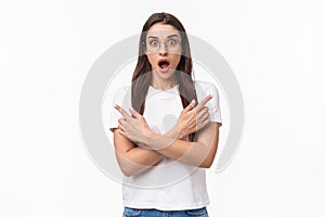 Waist-up portrait of amazed and astounded brunette 20s female in t-shirt, glasses, pointing fingers sideways, showing