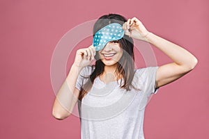 Waist up portrait of cheerful smiling girl in sleeping mask. Attractive funny female in stylish pajama standing and looking away.