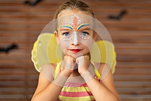Waist up portrait of cute preschooler with DIY face paint wearing a butterfly halloween or carnival costume.